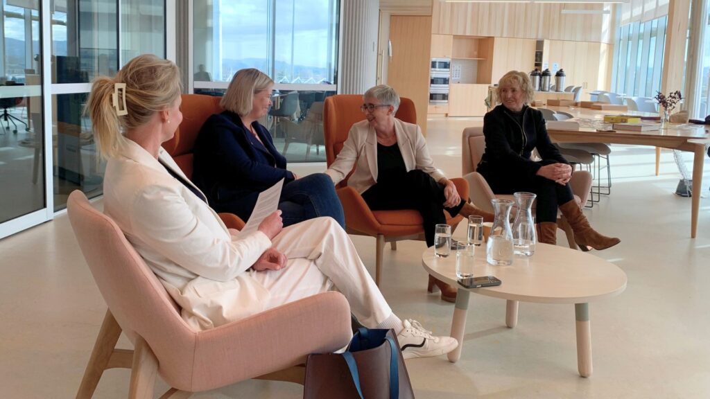 Four smartly dressed women sitting panel style in tub chairs, chatting in a semi-circle