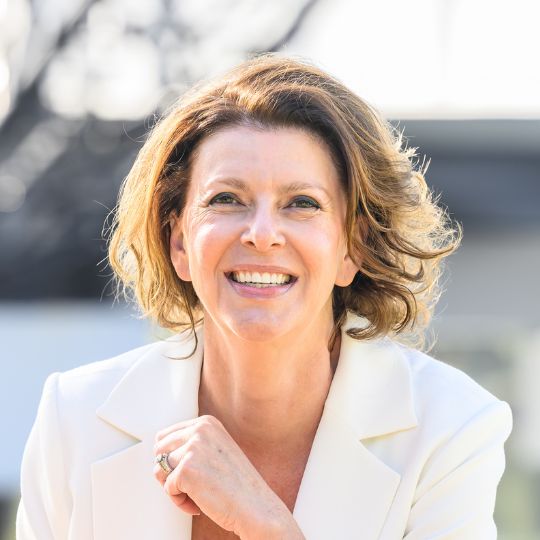 Smiling portrait of Catherine Lezer outdoors wearing a pale yellow blazer.