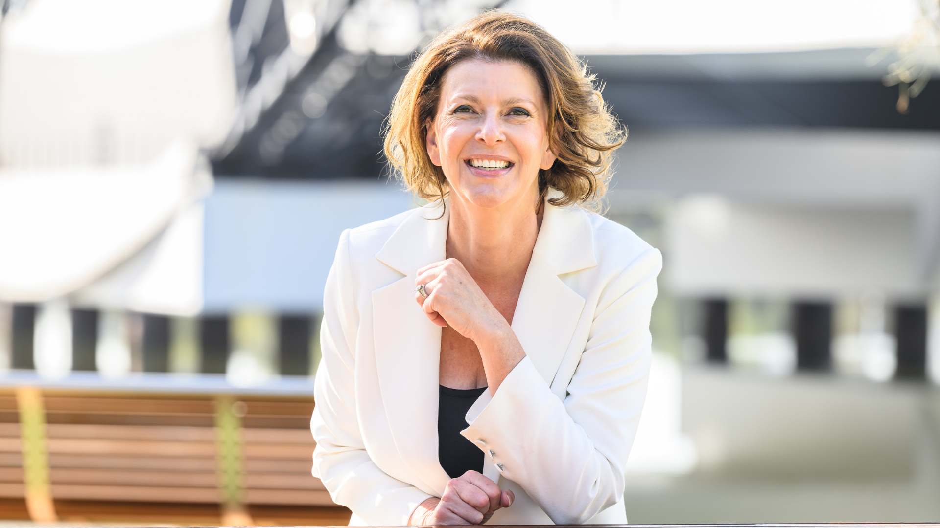 Smiling portrait of Catherine Lezer outdoors wearing a pale yellow blazer.