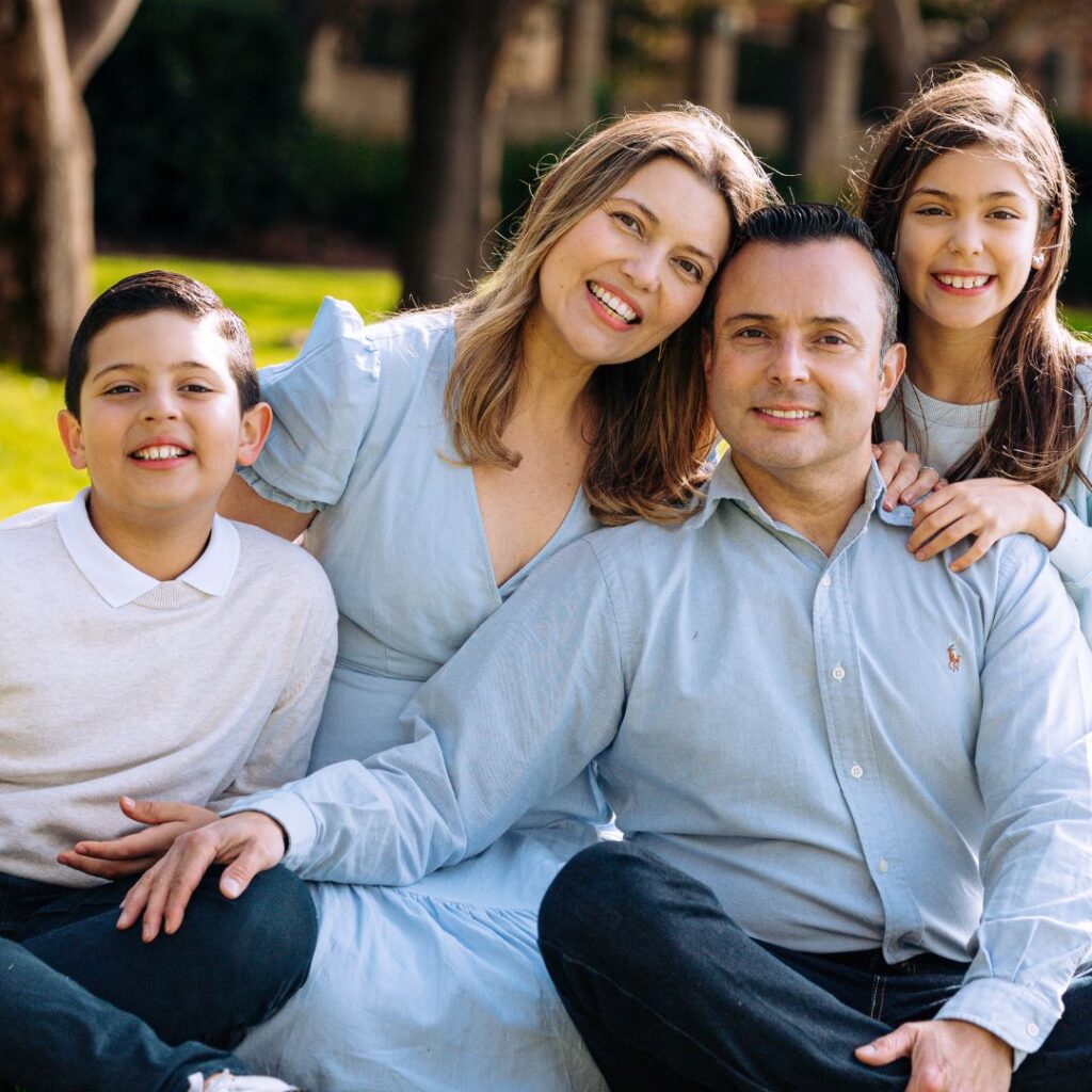 Dark haired smiling family pose sitting in the grass - a man, woman, boy and girl