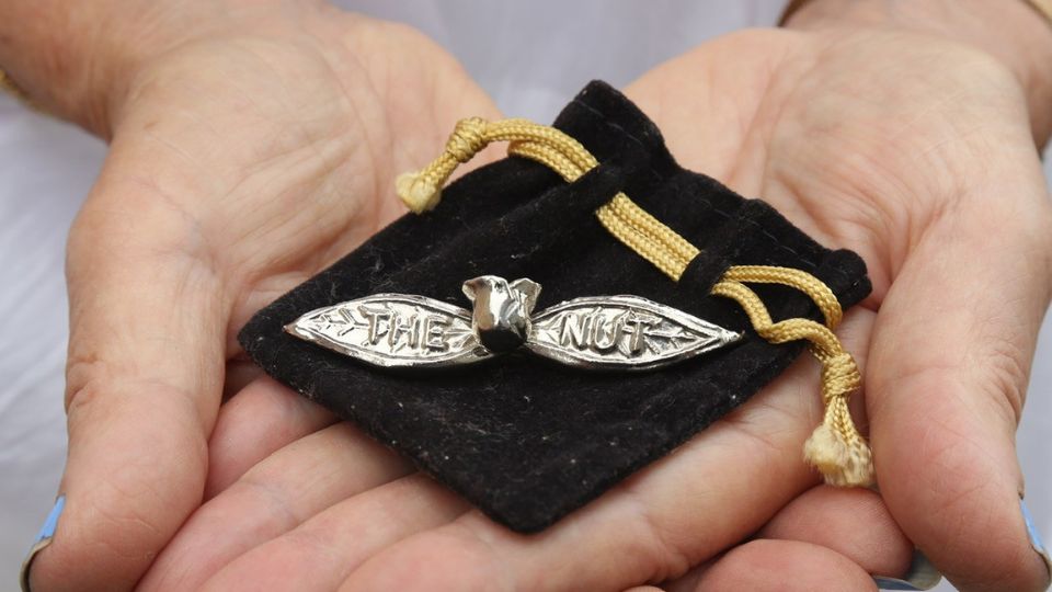 Hands holding out a silver  gumnut and leaf brooch engraved with the words "the nut"