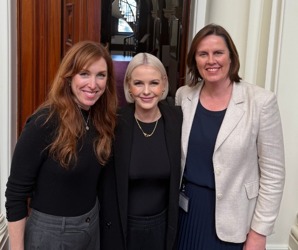 Three smiling women dressed in black and white business clothes, old wooden door behind them