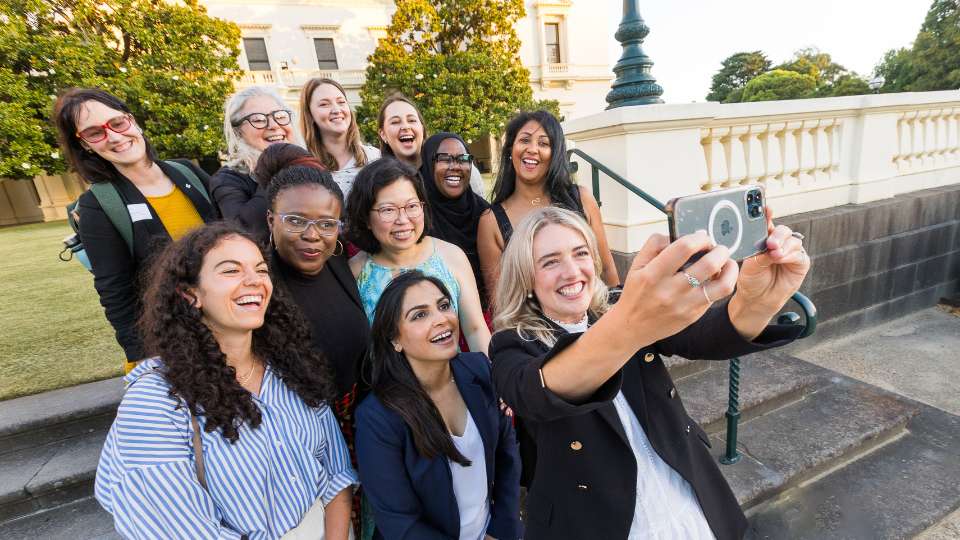 Group of diverse women taking a selfie, grand old buildings and garden in the background