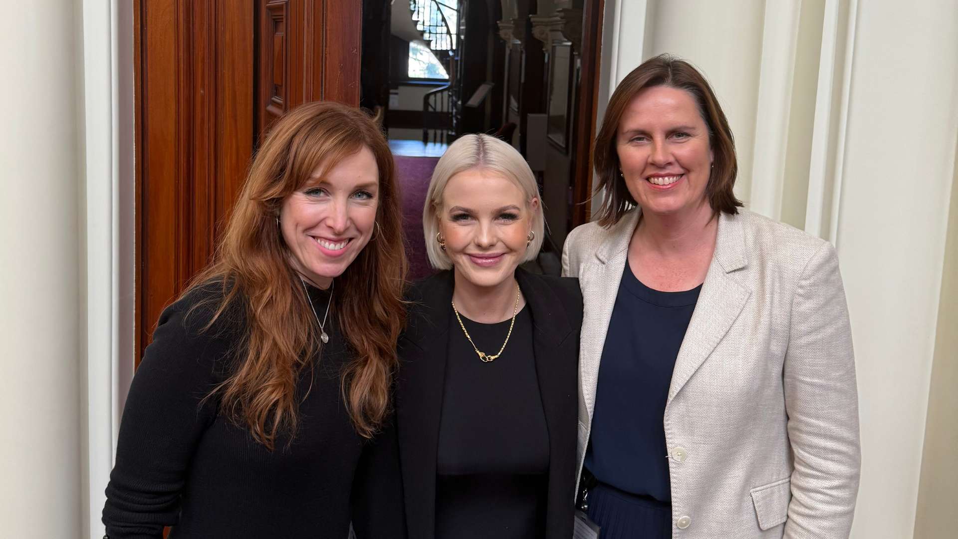Three women smiling in front of grand wooden door