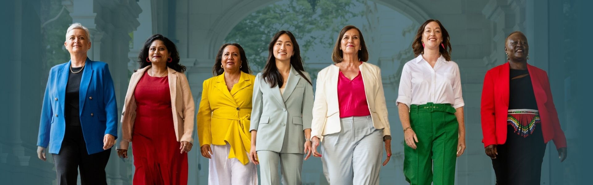 Photo of 6 diverse women wearing colourful business dress, striding forward in front of a parliamentary building