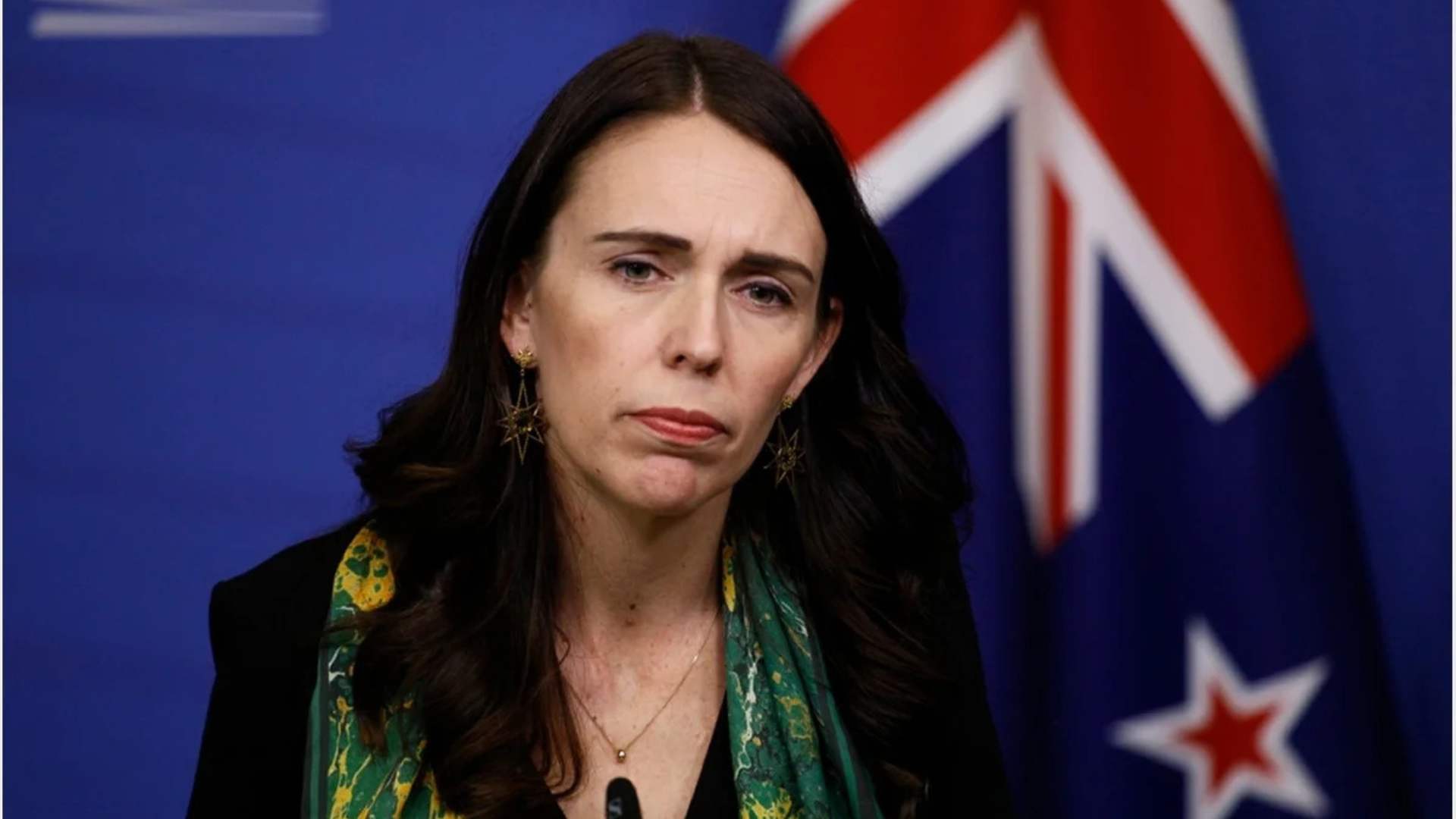 Photo of Jacinda Ardern, a concerned look on her face, New Zealand flag in the background