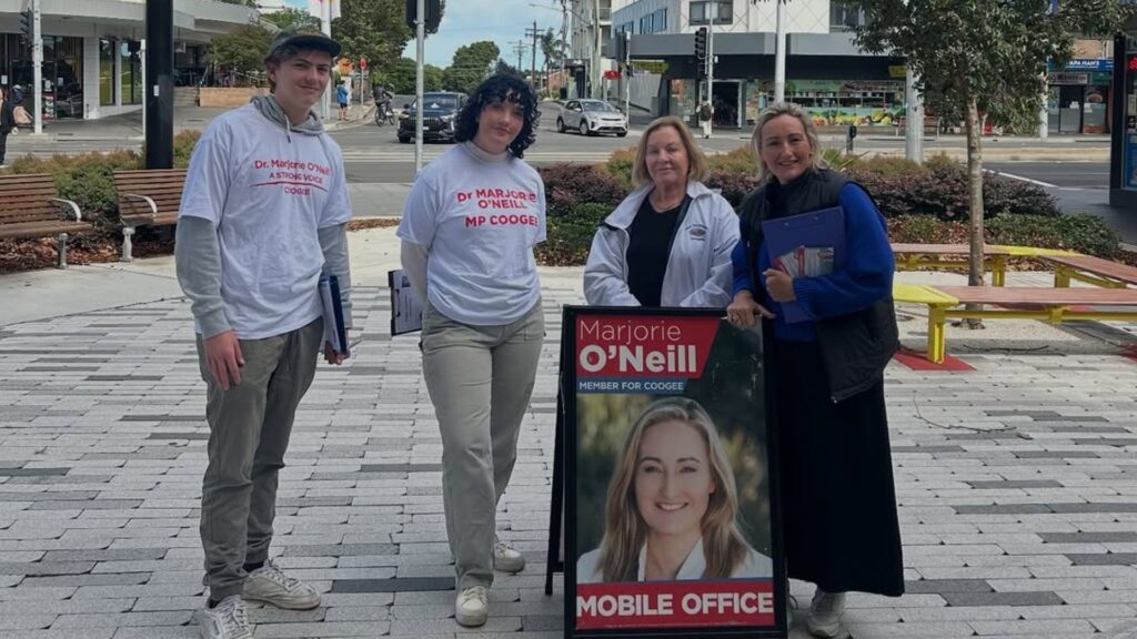 Photo of Keri and Marjorie in front of a Marjorie O'Neill Mobile Office sign, alongside two volunteers in white tshirts