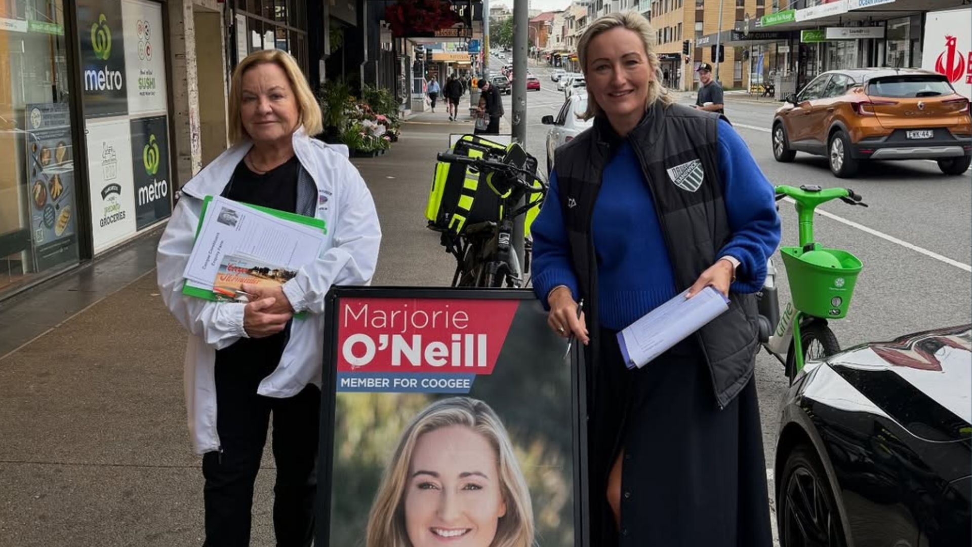 Photo of Ker and Marjorie in front of a Marjorie O'Neill Mobile Office sign,. They are outdoors in a high street location, dressed for cool weather.