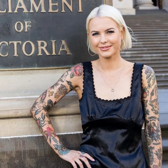 Photo of Georgie Purcell outside Victorian Parliament - bobbed blonde hair, tattooed arms