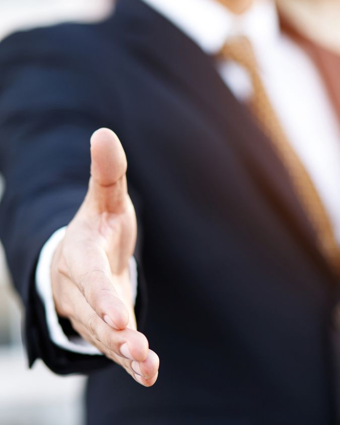 Torso of a man in a sharp suit, reaching forward to shake hands