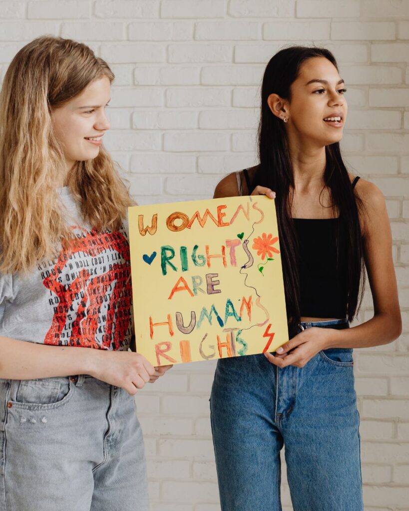 teen girls holding up a handmade sign that reads "womens rights are human rights"