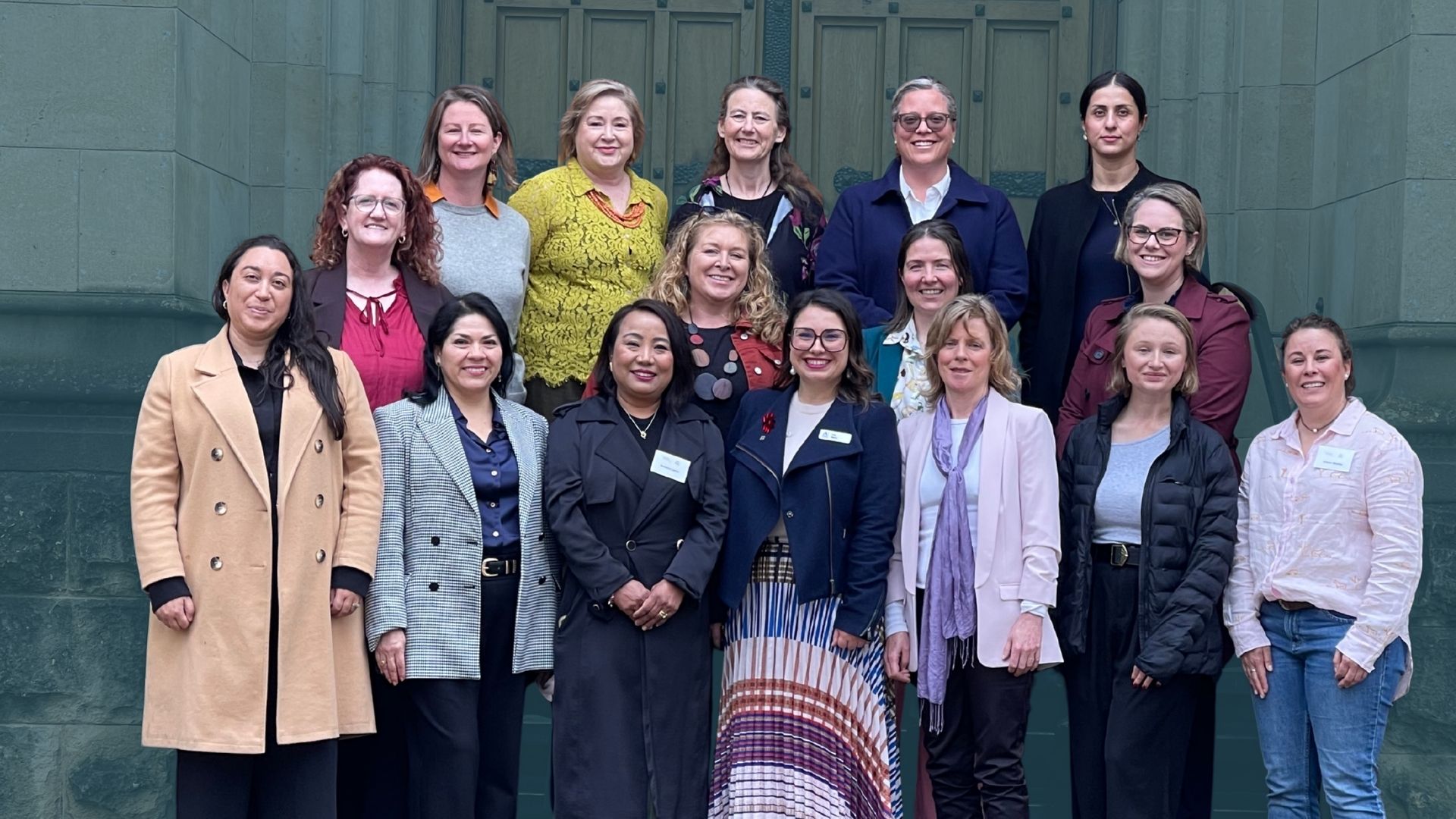 large group of diverse women smiling and posing for a photo in rows outside and old stone building