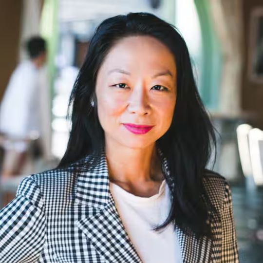 Smiling photo of Elisa, an Asian Australian woman wearing a black and white checked blazer