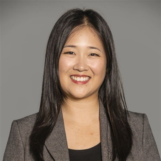 Smiling photo of Elisha, an Asian Australian woman with long straight hair, wearing a grey blazer
