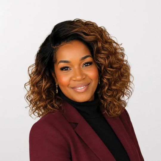 Smiling portrait of Jo, an African Australian woman with curly hair, wearing a burgundy blazer