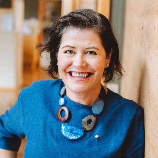 Photo of Ruth, a smiling caucasian woman wearing a blue blouse and chunky necklace